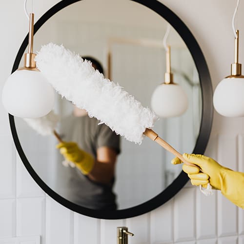 Feather dusting a mirror in a bathroom with gloves on